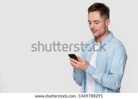 Young man interested looking at smartphone typing message chatting online. Millennial guy isolated on white grey blank copy space studio background. Social media, app, advertisement, tech concept