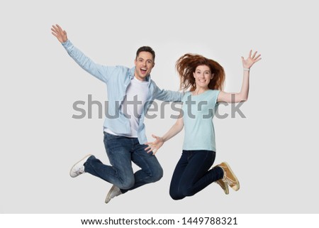 Crazy young handsome man and redhead millennial woman jumping high together with raised hands and bent in knees legs, happy, euphoric, energetic friends isolated on white grey studio background.