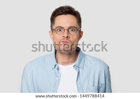 Headshot of confused angry man in eyeglasses looking at camera. Portrait of frustrated stylish male emotionally pressing his lips with furious look wearing glasses. Model posing for studio photoshoot
