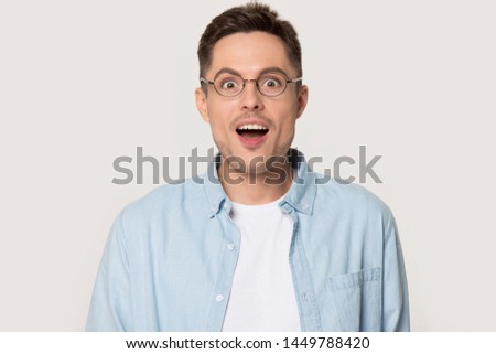 Surprised millennial man with eyes wide open looking at camera. Astonished male model posing at photoshoot in studio isolated on grey background wearing glasses. Advertising, sale copy space concept