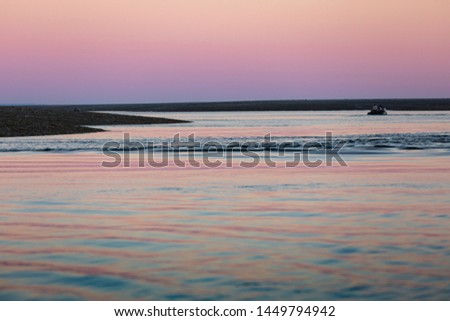 soft, long water surface ripples in a pink and silber sunset light, with a shiny horizon