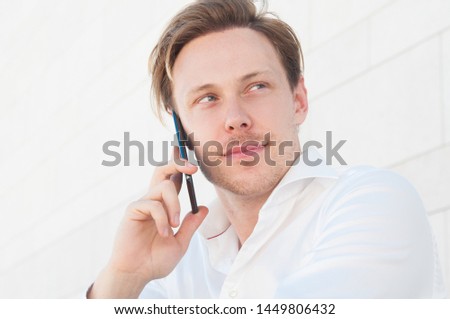 Pensive business man calling on smartphone outdoors. Guy using mobile phone with building wall in background. Communication in business concept. Front view.