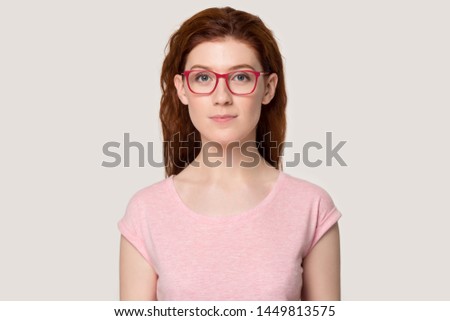 Head shot portrait millennial happy satisfied calm red-haired woman in eyeglasses. Confident focused attractive young girl looking at camera, posing for photo on grey white studio background.