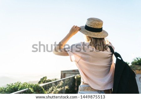 Banner with copy space. Close up of young fit female with backpack, sunset light and mountains on background. Girl traveler enjoying holidays and nature. woman holds her hat and looking at horizon 