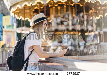 Side view of a young pretty girl in a hat with a phone in her hand. Young attractive millennial modern woman looks at her cell phone. Female taking picture or selfie on holidays. Summer freedom mood