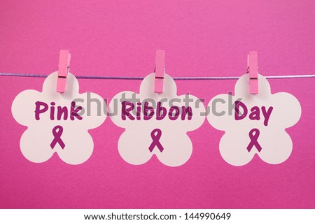 Pink Ribbon Day message greeting written across white flowers hanging from pink pegs on a line against a pretty feminine pink background.