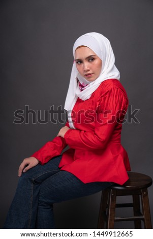 Fashionable female model in jeans, red blouse with hijab isolated on grey background. Studio hijab fashion and beauty concept