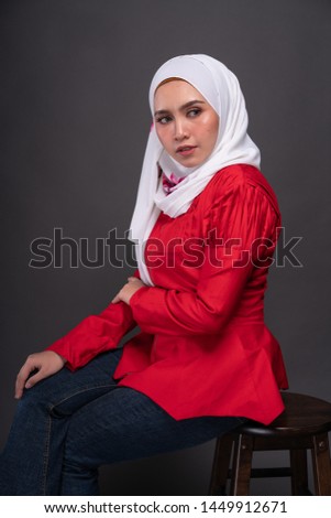 Fashionable female model in jeans, red blouse with hijab isolated on grey background. Studio hijab fashion and beauty concept