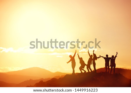 Big group of happy friends or big family silhouettes stands and having fun at sunset mountains. Space for text