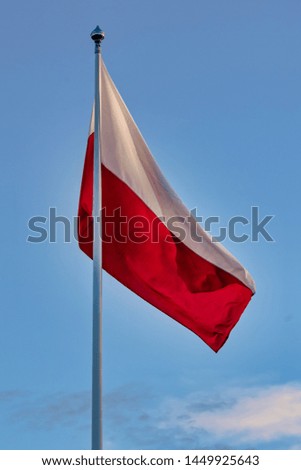 Polish flag in red and white colors waving in the evening sun.