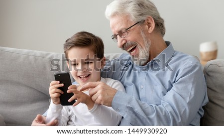 Happy grandfather and little grandson using phone, have fun together at home, laughing grandparent and cute preschool grandchild watching funny video, playing game, looking at cellphone screen Royalty-Free Stock Photo #1449930920