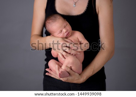 Mother kissing and hugging newborn son at gray background, tender, care, love. Portrait of woman and little baby, happiness concept, isolated image