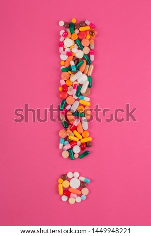 Exclamation mark arranged from assorted pharmaceutical medicine pills, tablets and capsules on pink background