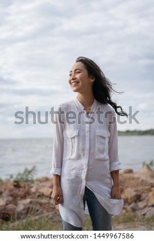 Cheerful asian woman with happy emotional face and beautiful smile standing near river. Authentic portrait of cute Korean girl walking, enjoying sea landscapes, breathing fresh air. Positive lifestyle