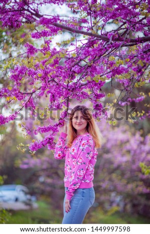 Young beautiful woman in a pink sweatshirt on a blooming tree with pink flowers background. Spring outdoors park.