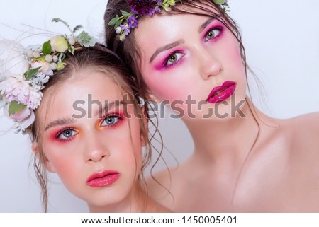 Bright and fashion spring art professional make-up for two beautiful sisters. Close up portrait. A hoop of fresh spring flowers peony on  heads. Model with clean skin, face care. Cosmetology for young
