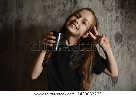 Little girl holding a coffee cup in black t-shirt. Mock up, perfect for putting your design on. Beautiful girl with long blond hair 9 years old drinks a drink from a black cup. A cute baby. teens