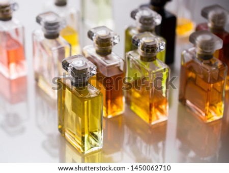 Perfume bottles, cologne, eau de parfum or toilette water, fragrance for man and woman. A lot of rectangle shape bottle with aromatic colored liquid, view with reflection on white glass table 