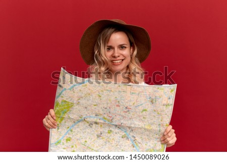 Happy blond girl with curly hair in a white t-shirt and a sundown hat looks at the map looking for itinerary while traveling. Concept of travel