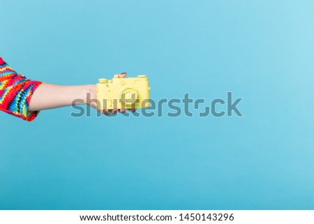 Photographing and vintage concept - female hand with yellow retro camera on blue background with copy space