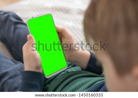 Smartphone with a hromakey in the hands of a child top view close up. Phone a for keying is holding kid. Smartphone with a green screen in hand child .
