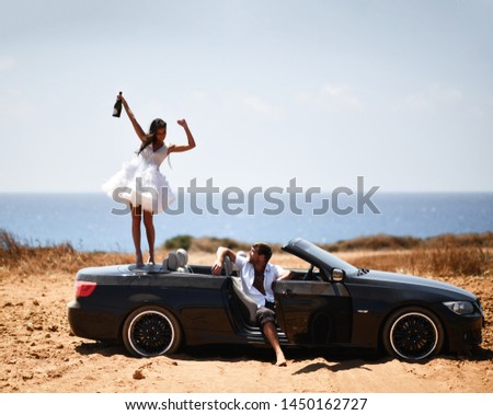 Happy cheerful couple party celebrating on cabrio car with champagne. Romantic vacation, honeymoon love story near the sea