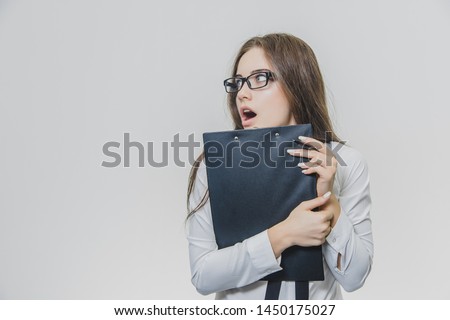 Adorable caucasian business woman is holding black paper holder or clipboard and looking at it with shock aside.
