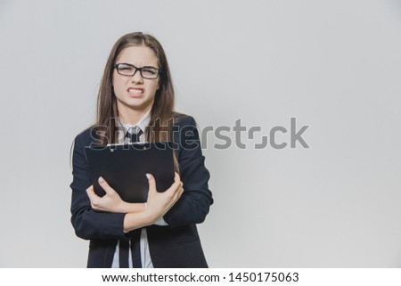 Adorable caucasian business woman is holding black paper holder or clipboard and looking at the camera being irritated and showing her perfect tooth.