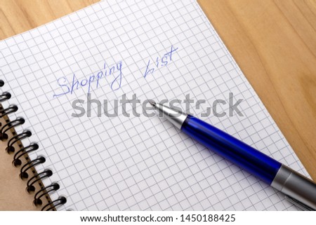Blue pen on a notebook with sheets in a cage. Sign Shopping List