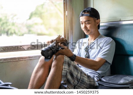 Asian man Traveler with check the image file from the camera, Sit on the old train seat at Thailand