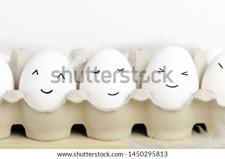 Kawaii face eggs in a carton with feathers on a white background close up. Concept cartoons, food decoration for children