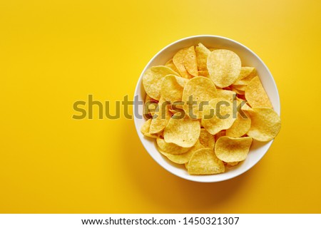 Close-up of potato chips or crisps in bowl against yellow background Royalty-Free Stock Photo #1450321307