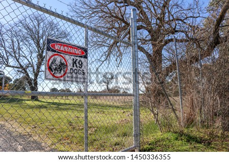 black, red and white Warning K9 Dogs, Enter With Caution danger sign on high wire gate and boundary fence