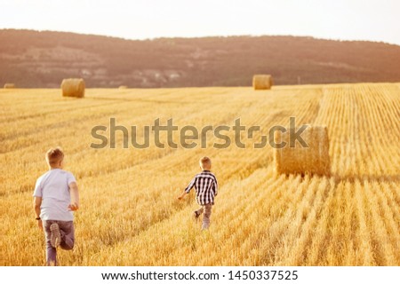 Two happy boys running together across the yellow field. Around the haystack.