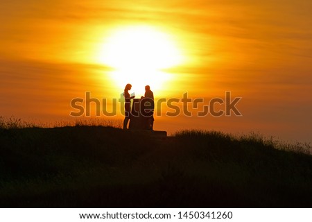 A couple silhouetted at sunset on Painswick Beacon in summer, The Cotswolds, Gloucestershire, England, UK
