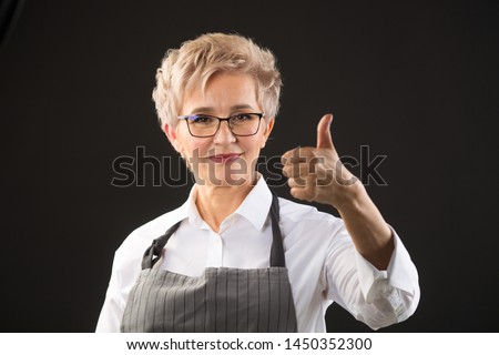 beautiful elderly woman in an apron and glasses on a black background with a gesture of hand