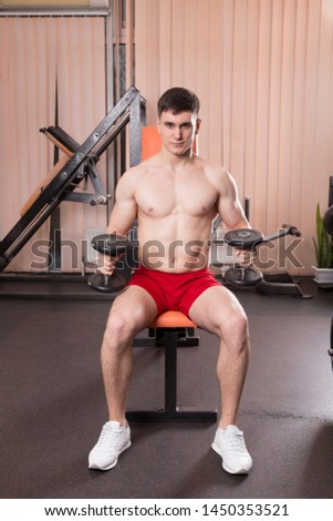 Young man flexing muscles with barbell in gym. Close-up.
