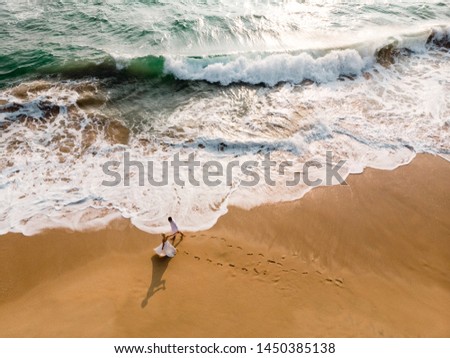 Picture from drone newlywed couple walking along beautiful beach. Scenic aerial view of Happy romantic couple waking together near the ocean. Wedding on the beach