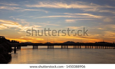 Darkness descends during the golden hour when the sun is setting in the night sky and the bridge and landscape are in silhouette