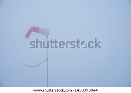 Wind vane or flag in dense fog with strong wind. Wind indicator is showing bad weather conditions for flying. Windsock