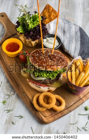 Burgers with juicy cutlet, onion rings, pickle, fresh vegetables,ketchup mayonnaise, crispy bun with sesame seeds on a wooden table. onion rings Traditional fast food.