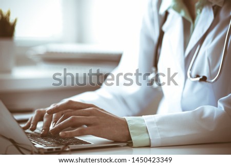 Doctor woman using laptop computer while sitting at the desk near window in hospital. Medicine and health care concept. Green is main color