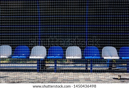Empty area for spectators of the sports ground. Spectator and coach area, empty blue and white plastic chairs behind the safety net. Place for text, front view.