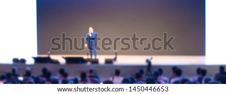 Blurred business presentation with keynote speaker near blank white screen. Seminar concept background with executive leading workshop in conference hall. Presenter in lecture to audience.

