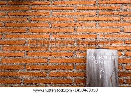 "Entrance Only" sign on wooden plank in English and Japanese texts leaning against orange brick wall.