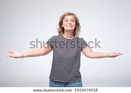 Cheerful european mature woman welcoming you with her arms outstretched out. Studio shot