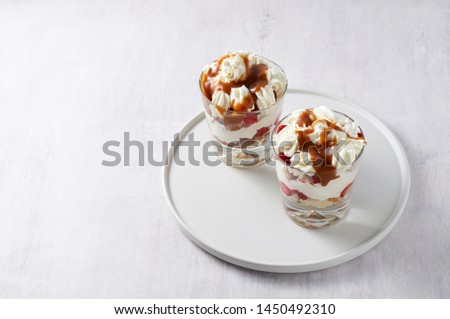 Layered dessert Trifle with vanilla cake, whipped cream, salted caramel and fresh strawberry. Two portion in glass on white background. Close up view with copy space