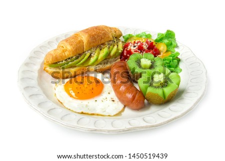 Breakfast set with croissant inside avocado salad black pepper, and fried egg, sausages, carved  tomato salad on topped sesame, fresh kiwi carved style in dish for healthy diet food fusion eat daily 