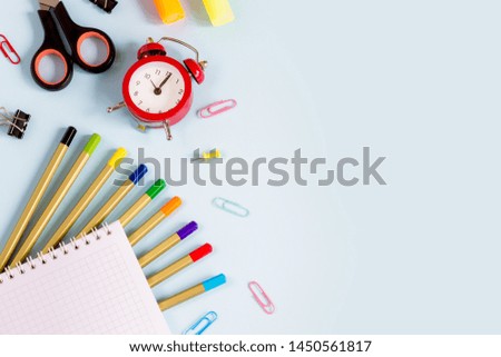 School supplies on a blue background with copy space for design. Pencils, scissors, notebook, alarm clock, top view. Back to school