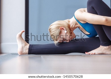 Healthy slim young girl doing marichiasana sitting on the rug on the floor in the hall during yoga. The concept of strengthening the abdominal organs